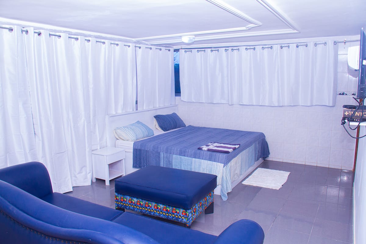A bedroom with a bed, a blue sofa, a small table, and a colorful ottoman.