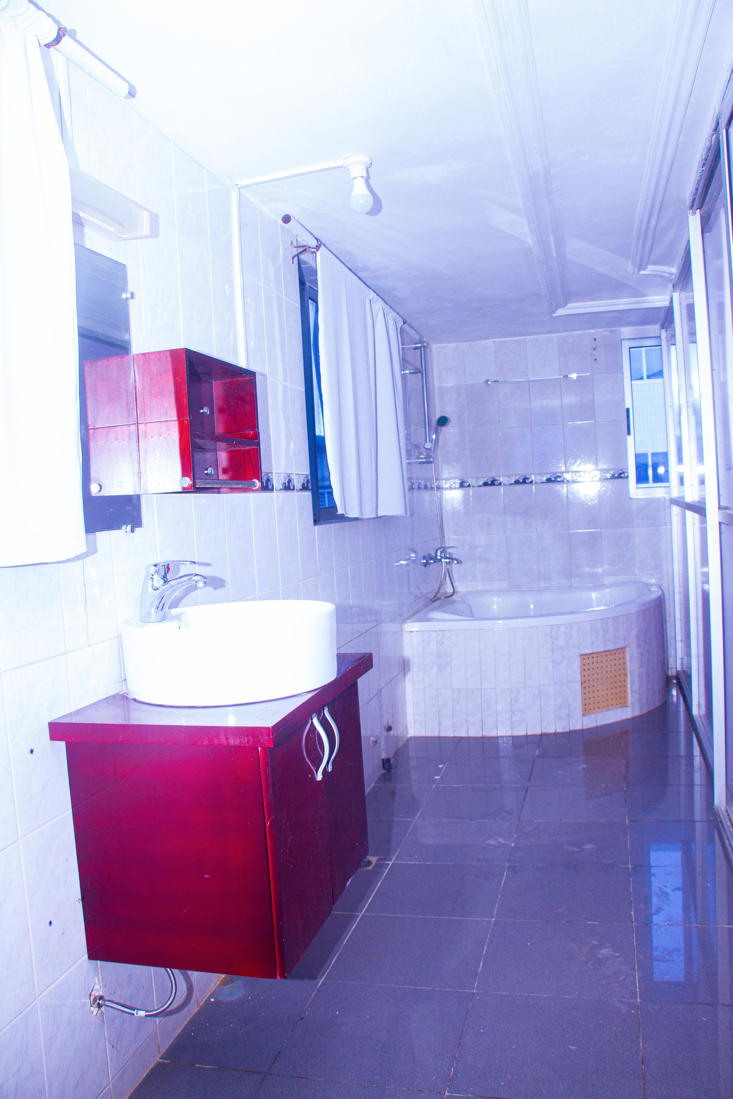 A bathroom with a white sink, red cabinet, and a large bathtub.