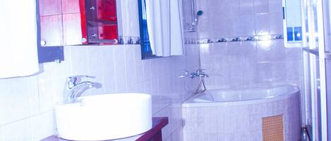 A bathroom with a white sink, red cabinet, and a large bathtub.