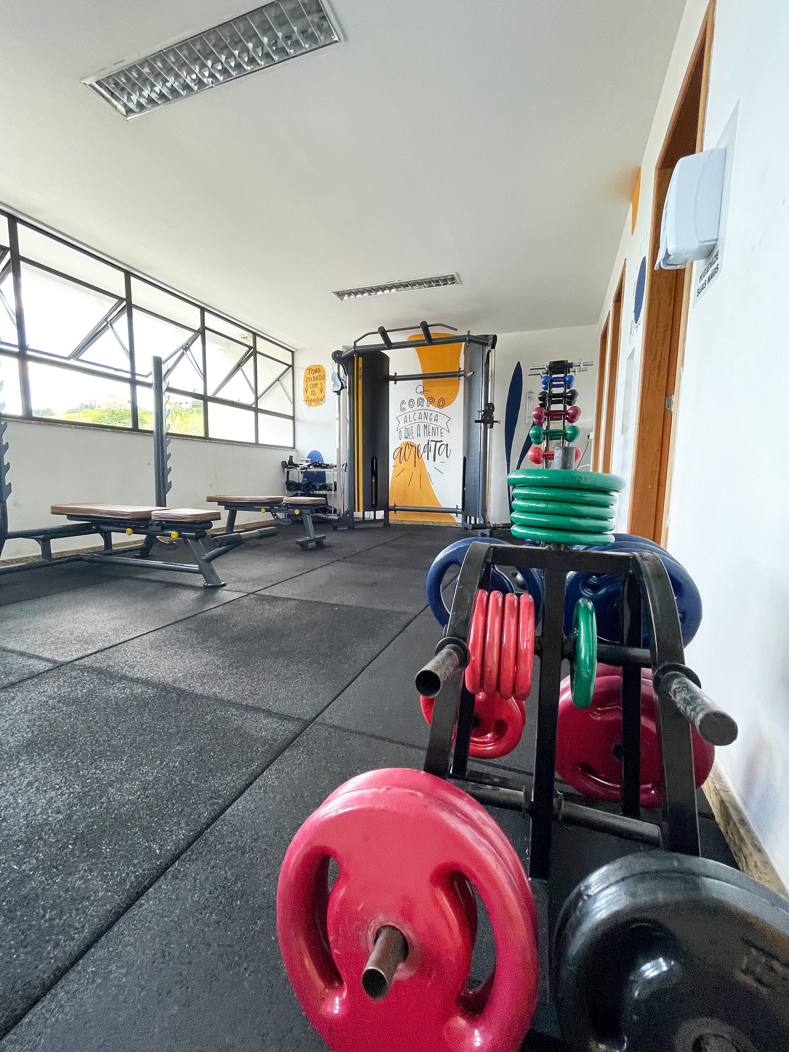Ett gym med utrustning för styrketräning, bänkar och ett stort fönster.