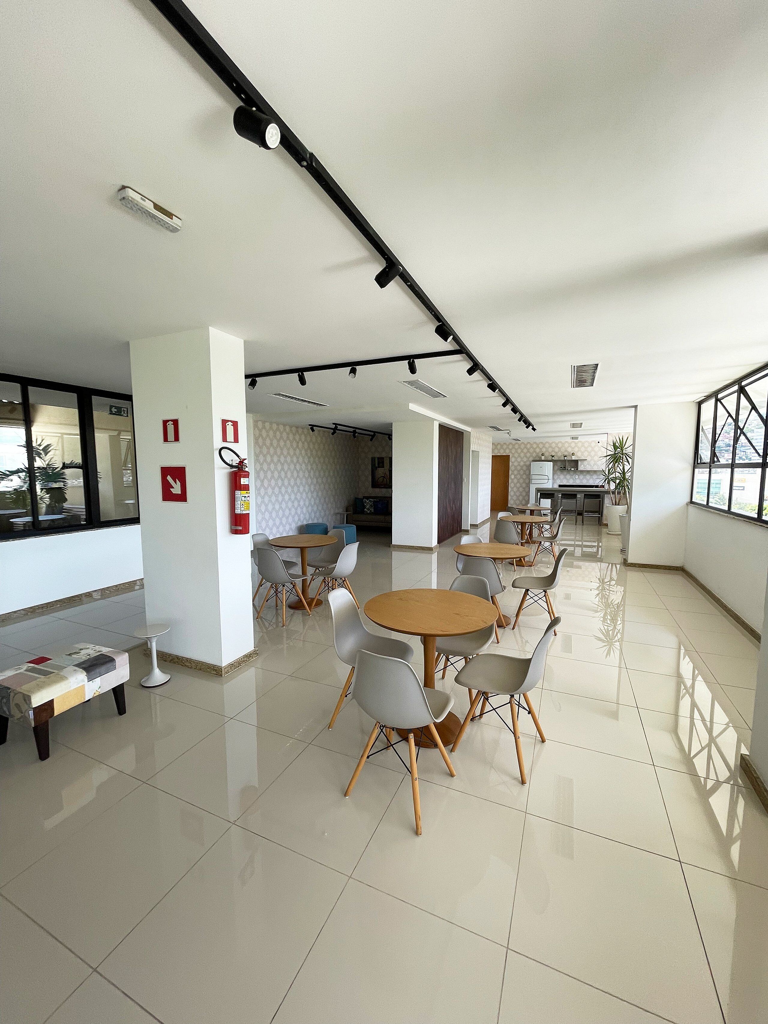 Amplio espacio interior con varias mesas y sillas, un extintor y una zona de cocina al fondo.