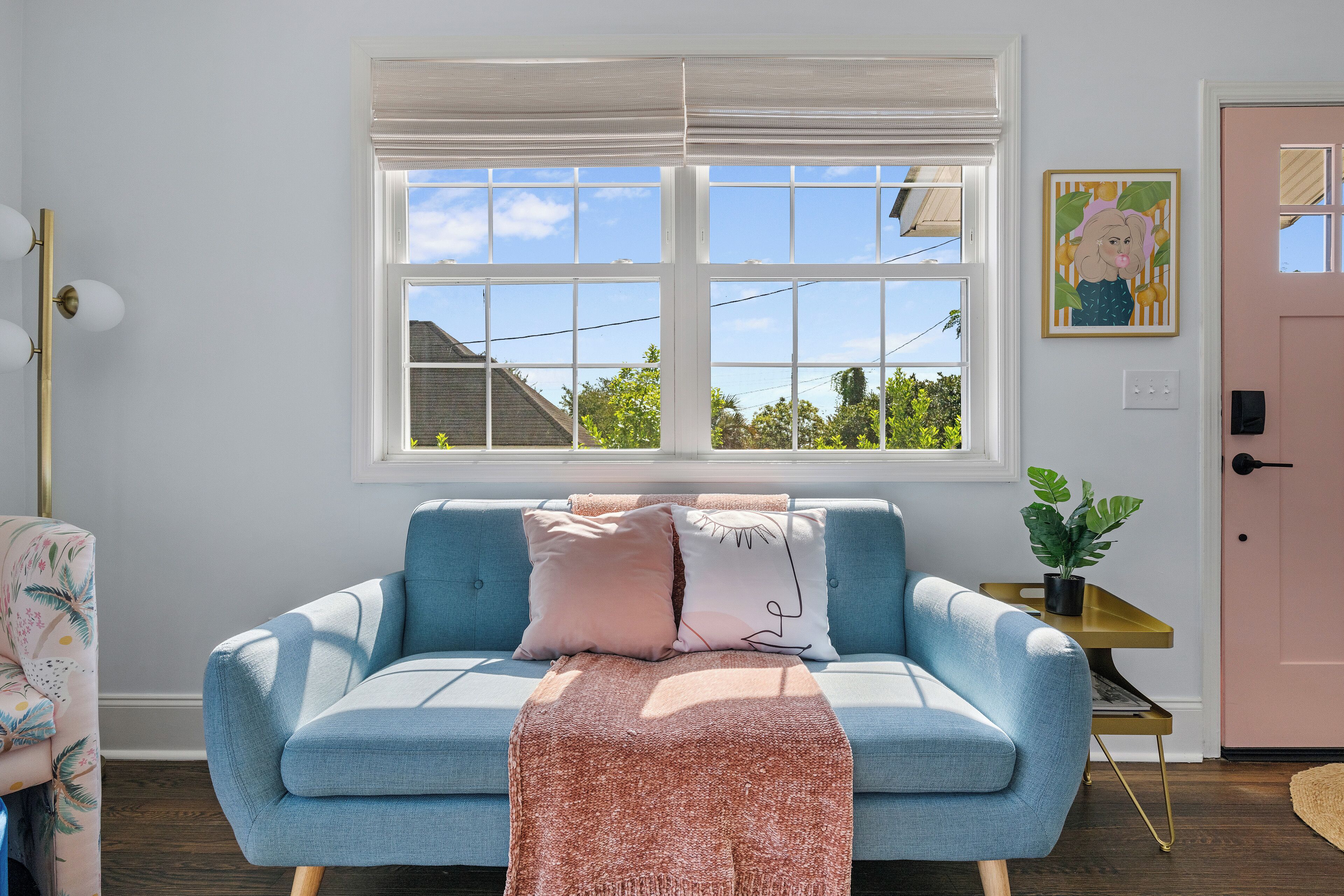 Ett rum med en blå soffa, en rosa dörr och ett fönster med utsikt över hus och träd.