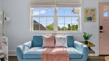Ett rum med en blå soffa, en rosa dörr och ett fönster med utsikt över hus och träd.