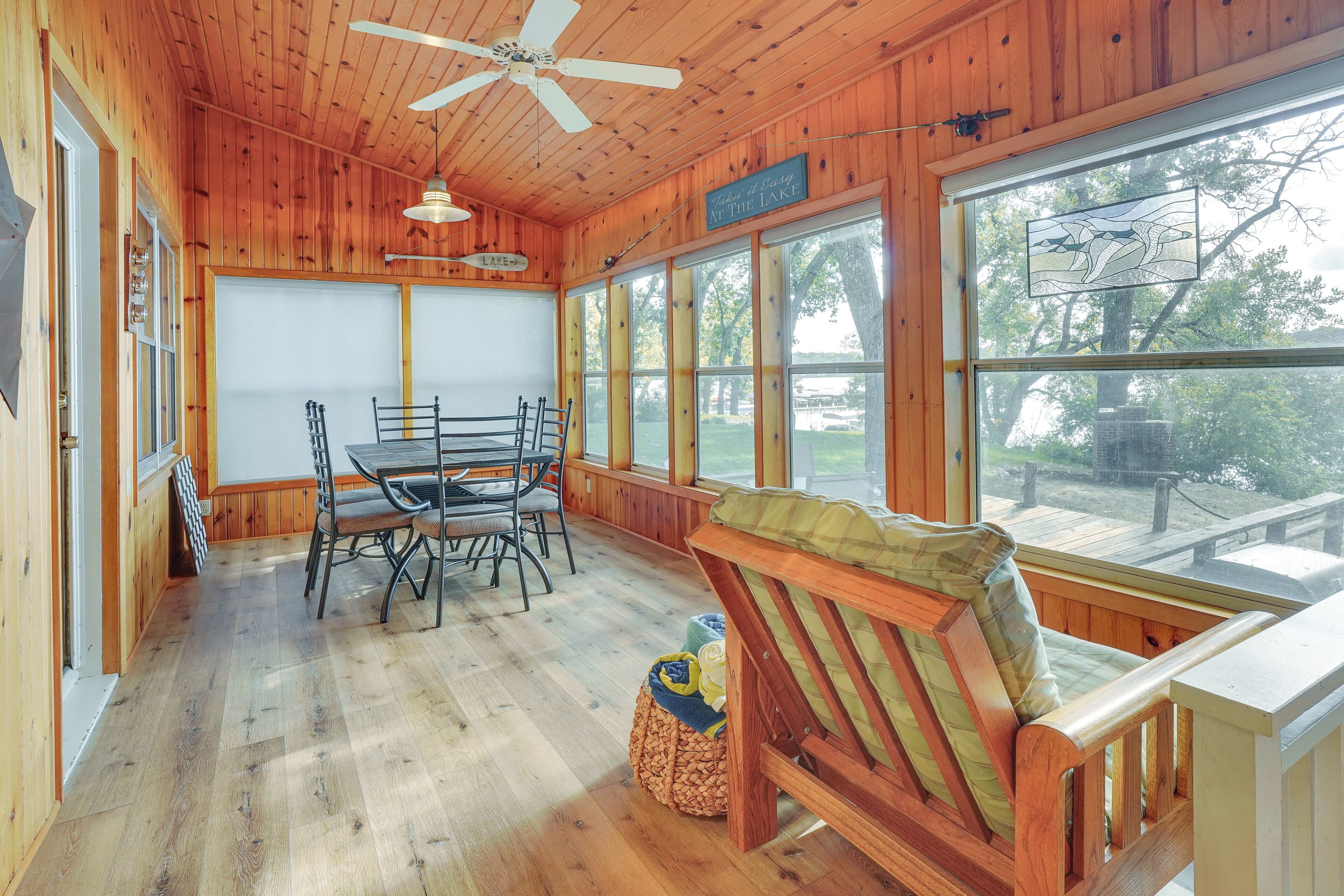 A wooden cabin with a dining area, a bench, and large windows overlooking a lake.