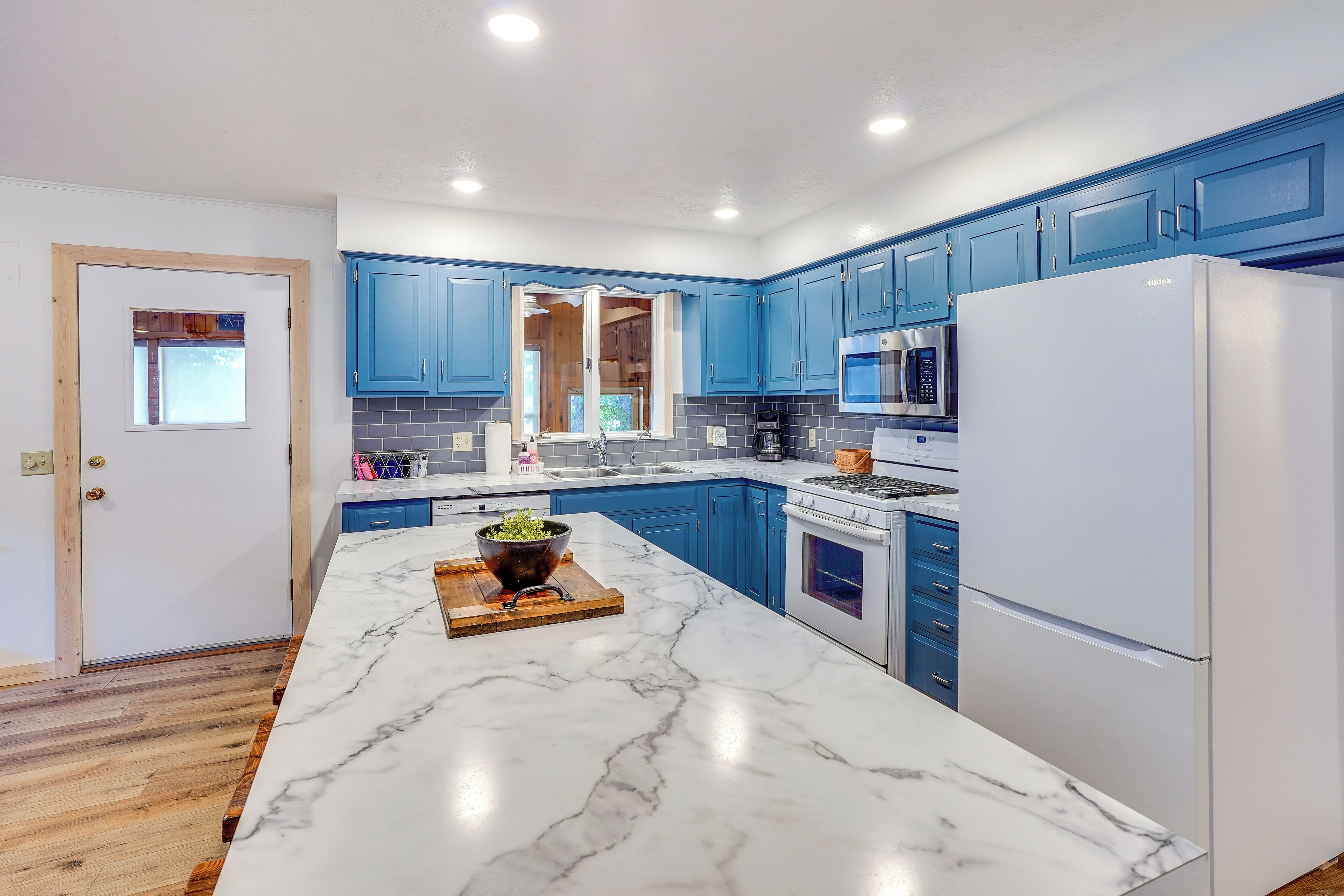 A modern kitchen with blue cabinets, white appliances, and a marble countertop.