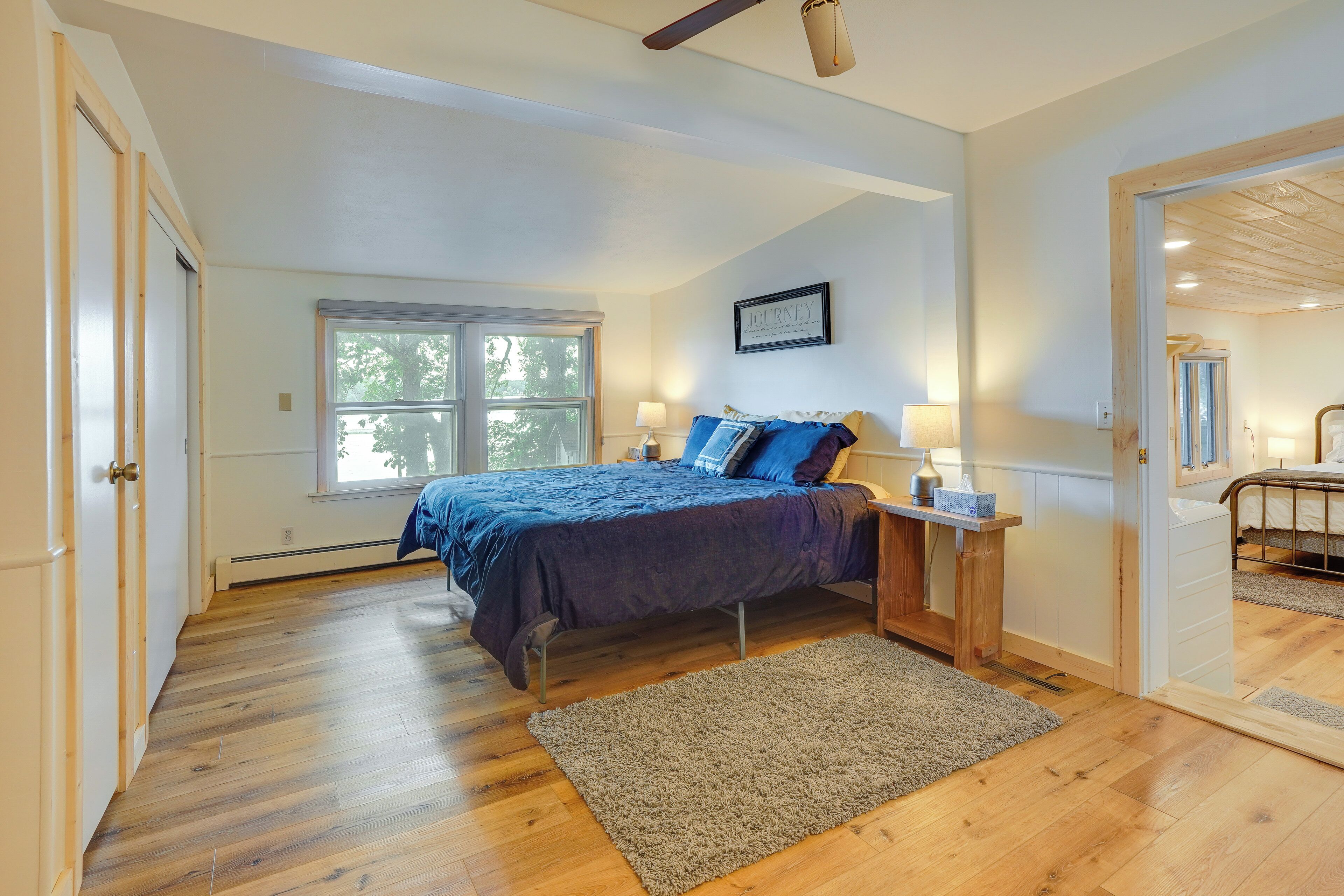 A bedroom with a large bed, a nightstand, a window, and a door leading to another room.