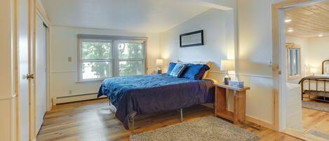 A bedroom with a large bed, a nightstand, a window, and a door leading to another room.