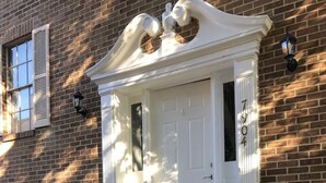 A brick building with a white front door, a small porch, and a black doormat. - Room in House - Modern Executive Master Bedroom (Alexandria)