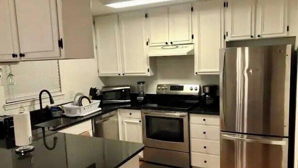A kitchen with white cabinets, a stainless steel refrigerator, an oven, a microwave, and a coffee maker. - Room in House - Modern Executive Master Bedroom (Alexandria)