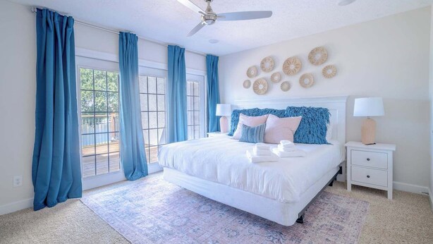 A bedroom with a large bed, a ceiling fan, and a view through the glass door. - Professionally designed lake stay for families, friends, and celebrations (Montgomery)