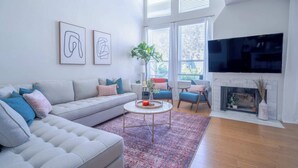 A modern living room with a grey sofa, two armchairs, a coffee table, and a fireplace. There are abstract wall art pieces and a large TV mounted on the wall. - Professionally designed lake stay for families, friends, and celebrations (Montgomery)