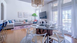 A modern living room with a glass dining table, a grey sofa, and a large window with curtains. - Professionally designed lake stay for families, friends, and celebrations (Montgomery)
