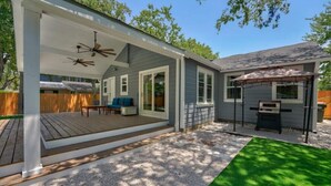 Una veranda riparata con ventilatore a soffitto, zona barbecue e terrazza in legno.