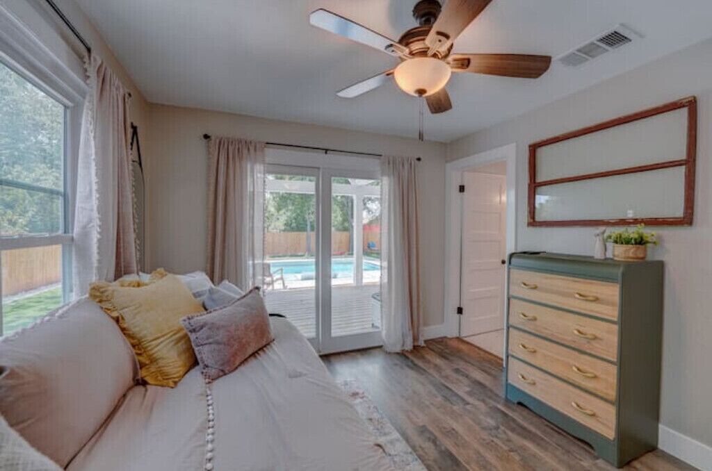 A bedroom with a bed, a dresser, a ceiling fan, and a sliding glass door leading to a backyard.