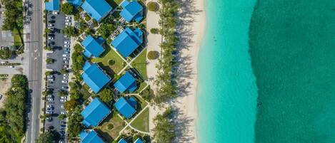An aerial view of a resort with multiple blue-roofed buildings, a beach, and a parking area.