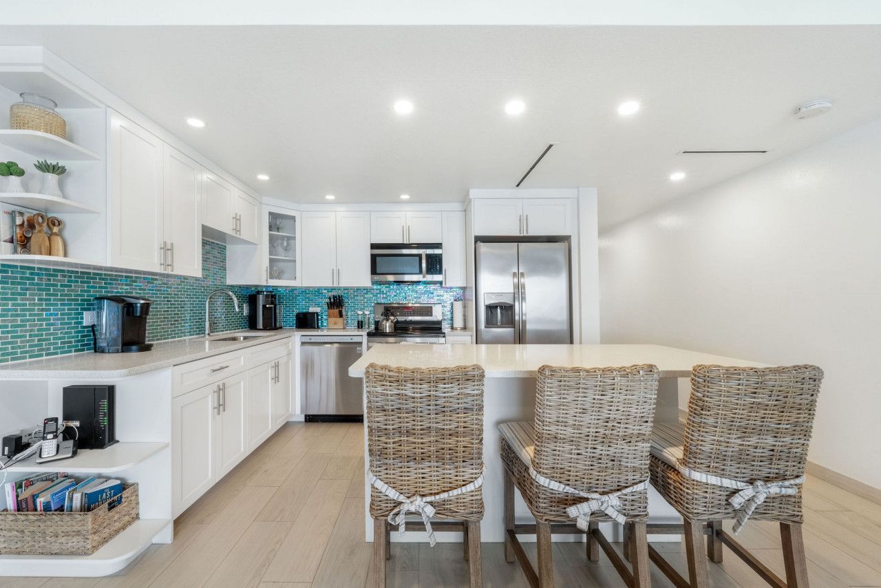A modern kitchen with white cabinets, a teal backsplash, and a central island with wicker chairs.