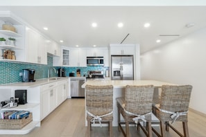 A modern kitchen with white cabinets, a teal backsplash, and a central island with wicker chairs. - In-Between Ritz Carlton and Westin | Oceanview 1BR on Seven Mile Beach (West Bay)