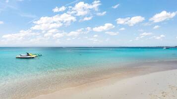 A beach with clear turquoise water, a sandy shore, and a small boat in the distance.