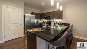 A modern kitchen with stainless steel appliances, a central island with bar stools, and pendant lighting. - Foothills G-204 (Branson)