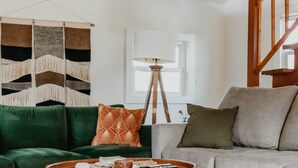 A room with a green sofa, a grey sofa, a round coffee table, a woven light fixture, and a wall tapestry.