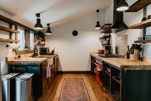Una cocina con suelo de madera, lámparas colgantes negras y un reloj en la pared.