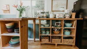 A kitchen with wooden shelves holding dishes, pots, and a coffee maker.