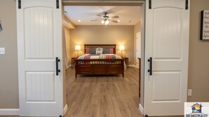 A bedroom with a bed, two bedside lamps, a ceiling fan, and a sliding barn door. - Foothills G-104 (Branson)
