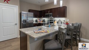 A modern kitchen with dark wood cabinets, stainless steel appliances, and a granite countertop. There are three pendant lights, a white door, and a star decoration on the wall. - Foothills G-104 (Branson)