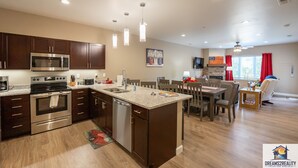A modern kitchen with stainless steel appliances, a dining area with a wooden table and chairs, and a living space with a fireplace and red curtains. - Foothills G-104 (Branson)
