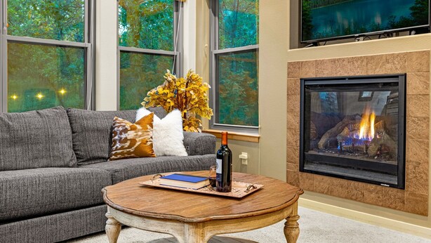 A living room with a fireplace, a sofa, a coffee table, and a TV mounted on the wall. - The Glen House, a lovely 4 bedroom home in Palmer Lake, with hot tub, and views! (Palmer Lake)