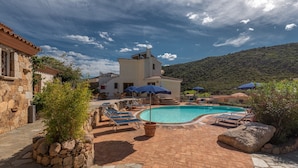 A pool area with lounge chairs and umbrellas, surrounded by stone walls and vegetation. - Stunning Residence Bouganvillage Studio N1306 (Budoni)