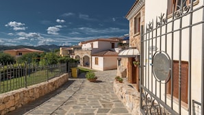A stone-paved courtyard with a metal gate, surrounded by buildings with terracotta roofs and stone walls. - Stunning Residence Bouganvillage Studio N1306 (Budoni)