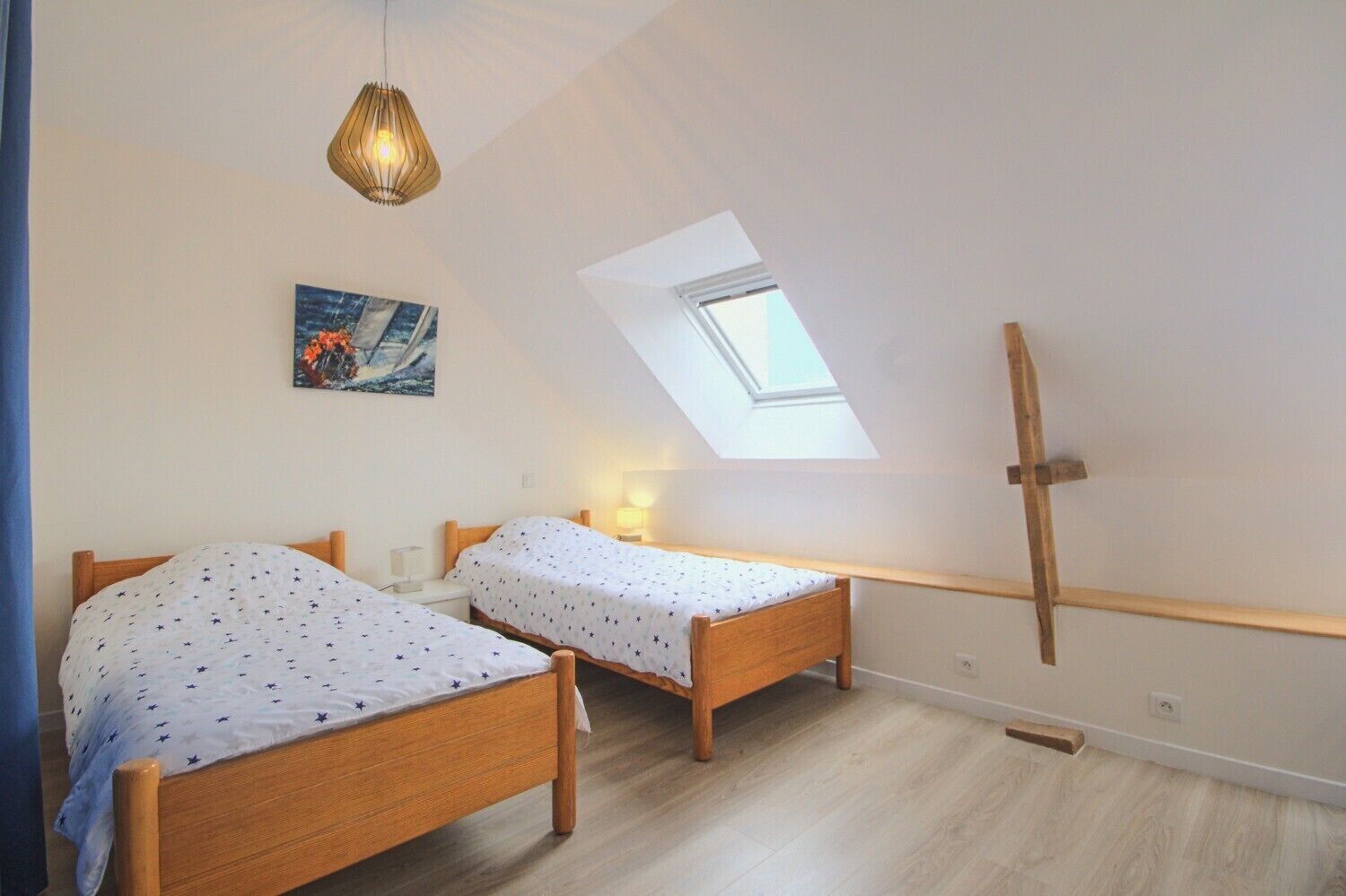 Un dormitorio con dos camas de madera, un tragaluz, un cuadro y una escalera de madera.