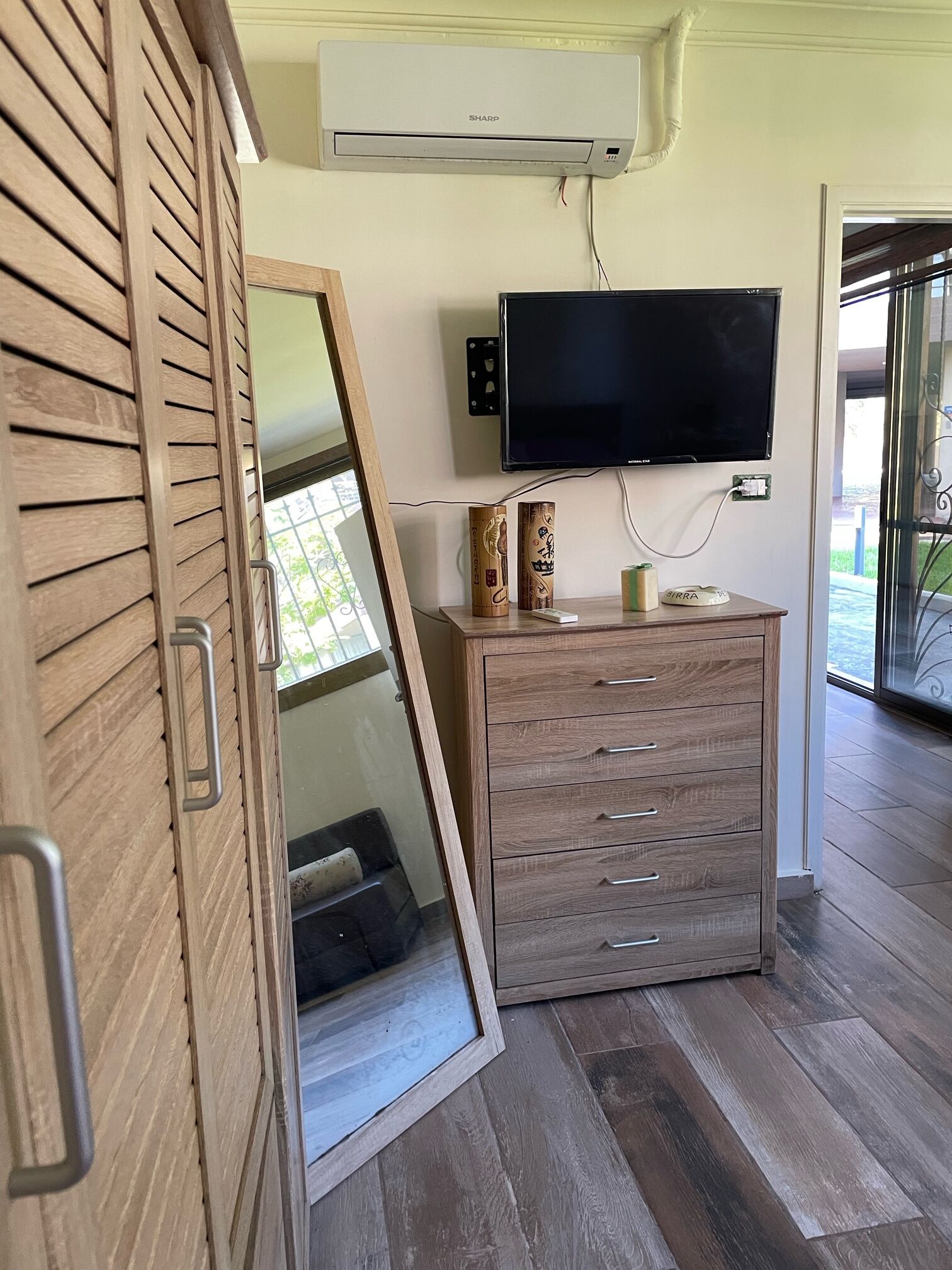 A room with a wooden cabinet, a mounted TV, and an air conditioning unit.