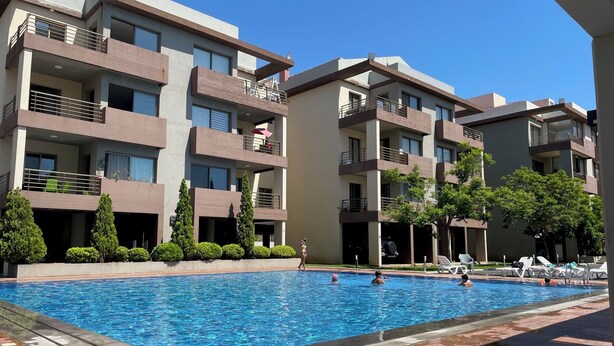 Un immeuble d’appartements moderne doté d’une piscine, de nombreux balcons et d’un espace jardin bien entretenu.