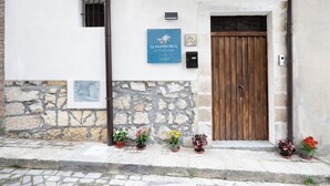 Fachada de edificio con pared de piedra, puerta de madera y letrero azul.
