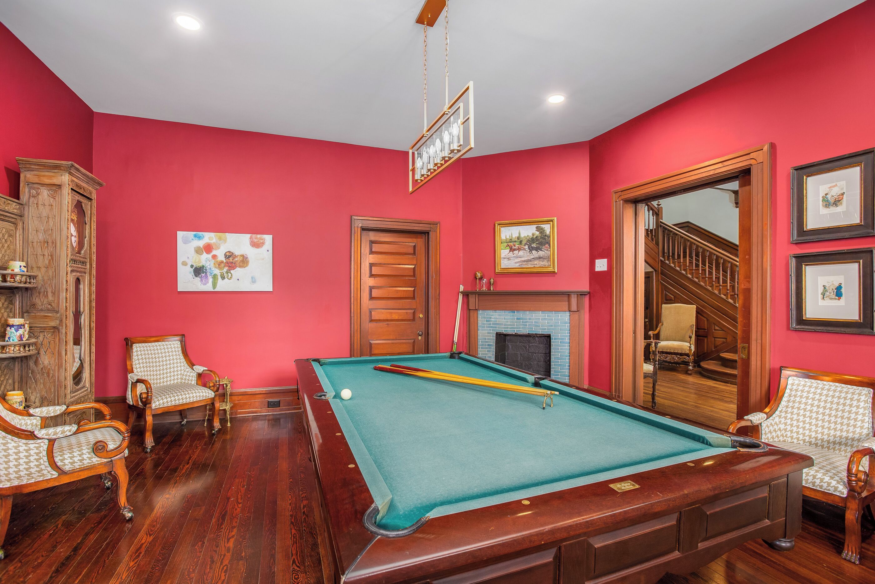 A room with a pool table, wooden chairs, a fireplace, and a staircase.