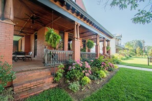 A covered porch with brick columns, outdoor seating, and a well-maintained garden with pink flowers.