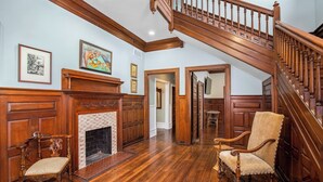 A spacious room with a wooden staircase, a fireplace, and two antique chairs. - Summit Street Inns (Winston-Salem)