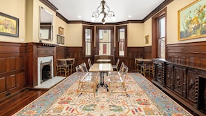 A dining room with a large table, clear chairs, a patterned carpet, wooden paneling, and a chandelier. - Summit Street Inns (Winston-Salem)
