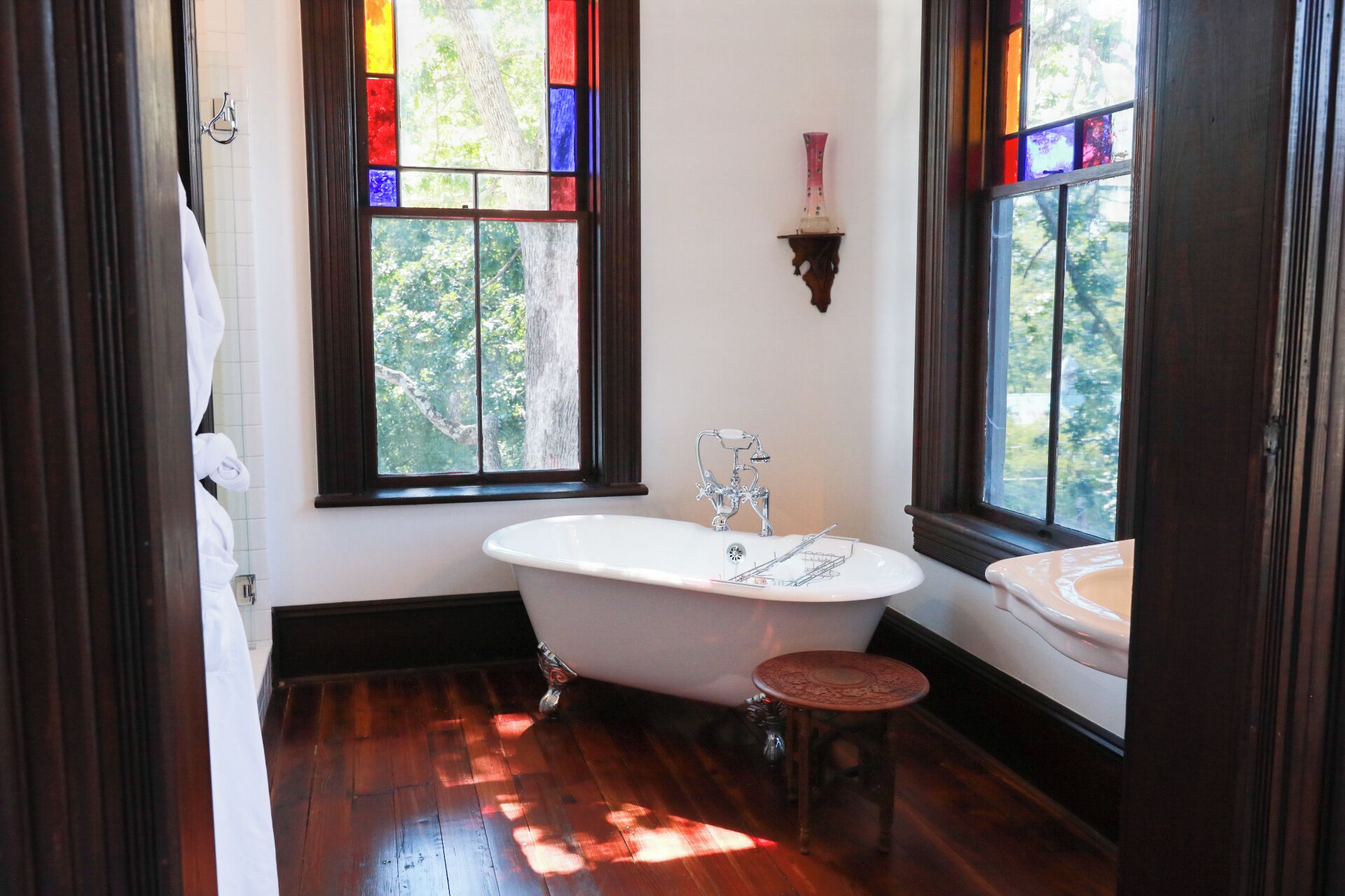 A bathroom with a freestanding bathtub, a sink, and a window with stained glass.