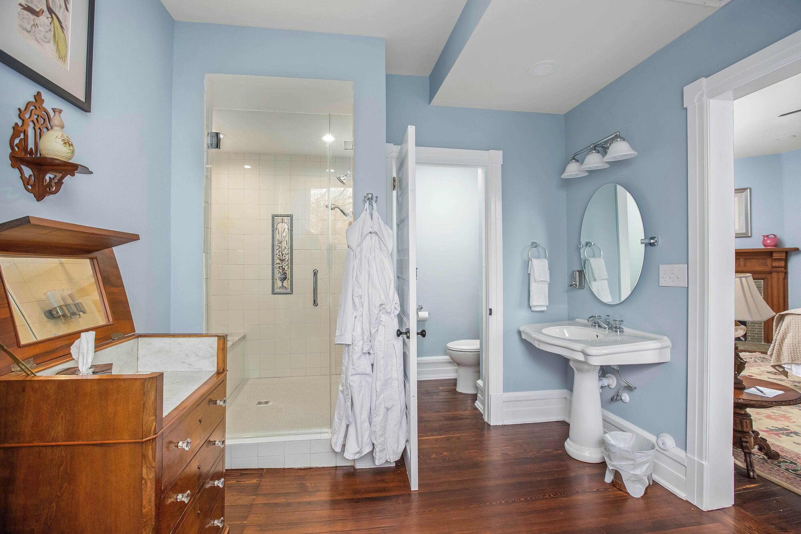 Une salle de bain avec une commode en bois, un lavabo blanc, un miroir et un espace douche.