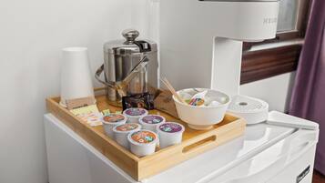 A coffee machine, a coffee pot, and a tray with coffee cups and a bowl on a white counter.