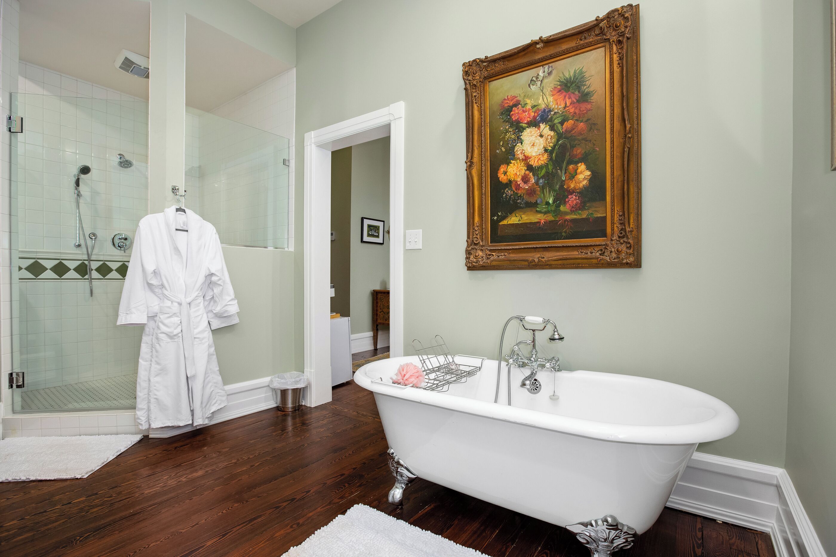 Ein Badezimmer mit einer weißen Badewanne, einer Duschkabine aus Glas und einem gerahmten Blumenbild an der Wand.