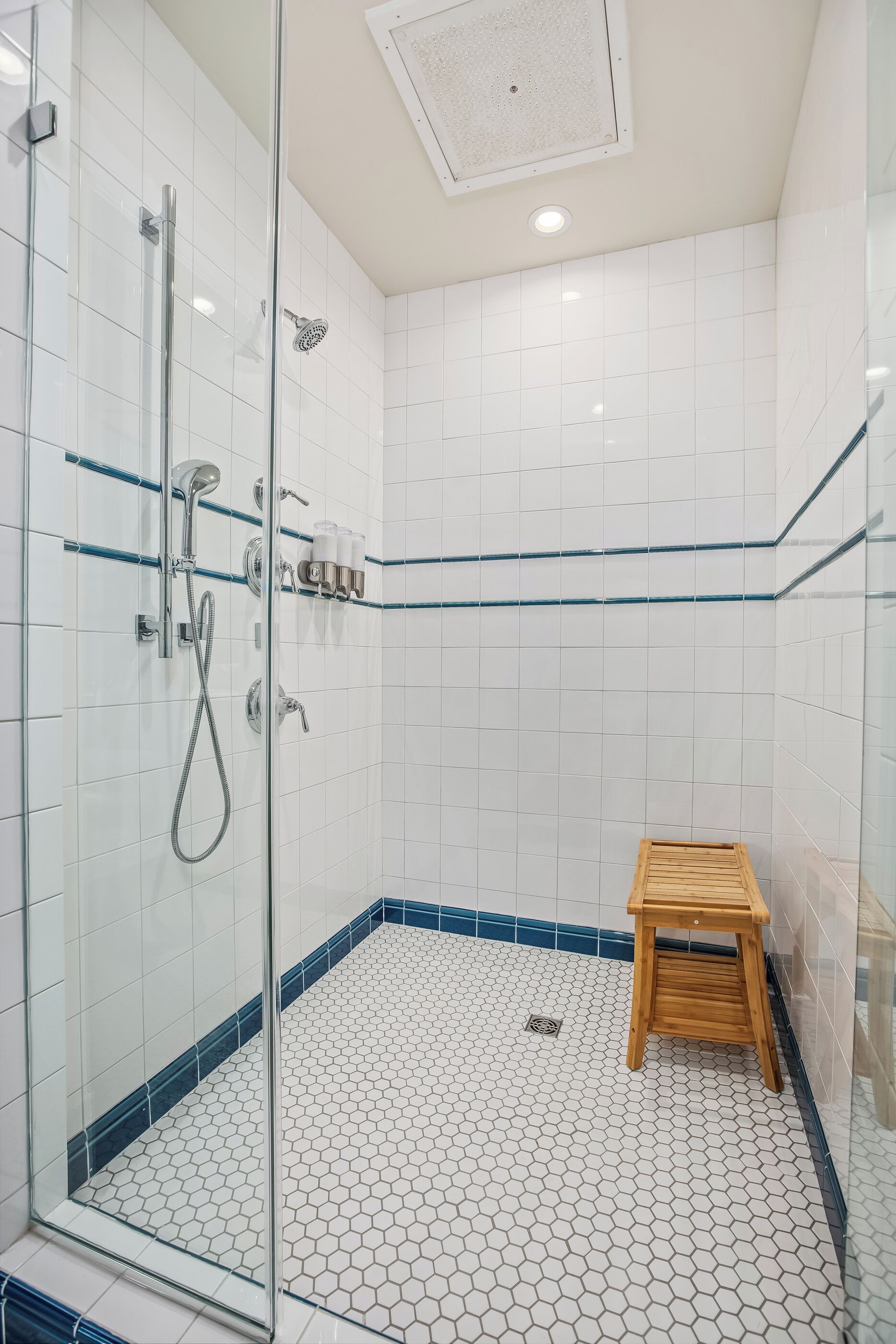 Une salle de bain moderne avec une douche à parois de verre, des carreaux hexagonaux blancs et un tabouret en bois.
