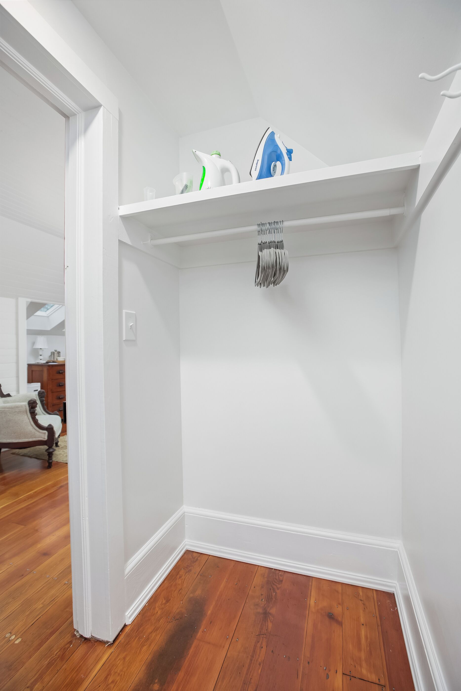 A corner of a room with a white wall, a wooden floor, and a white shelf with a blue iron and a white appliance.