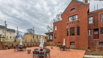 A courtyard with outdoor seating, brick buildings, and a white picket fence.