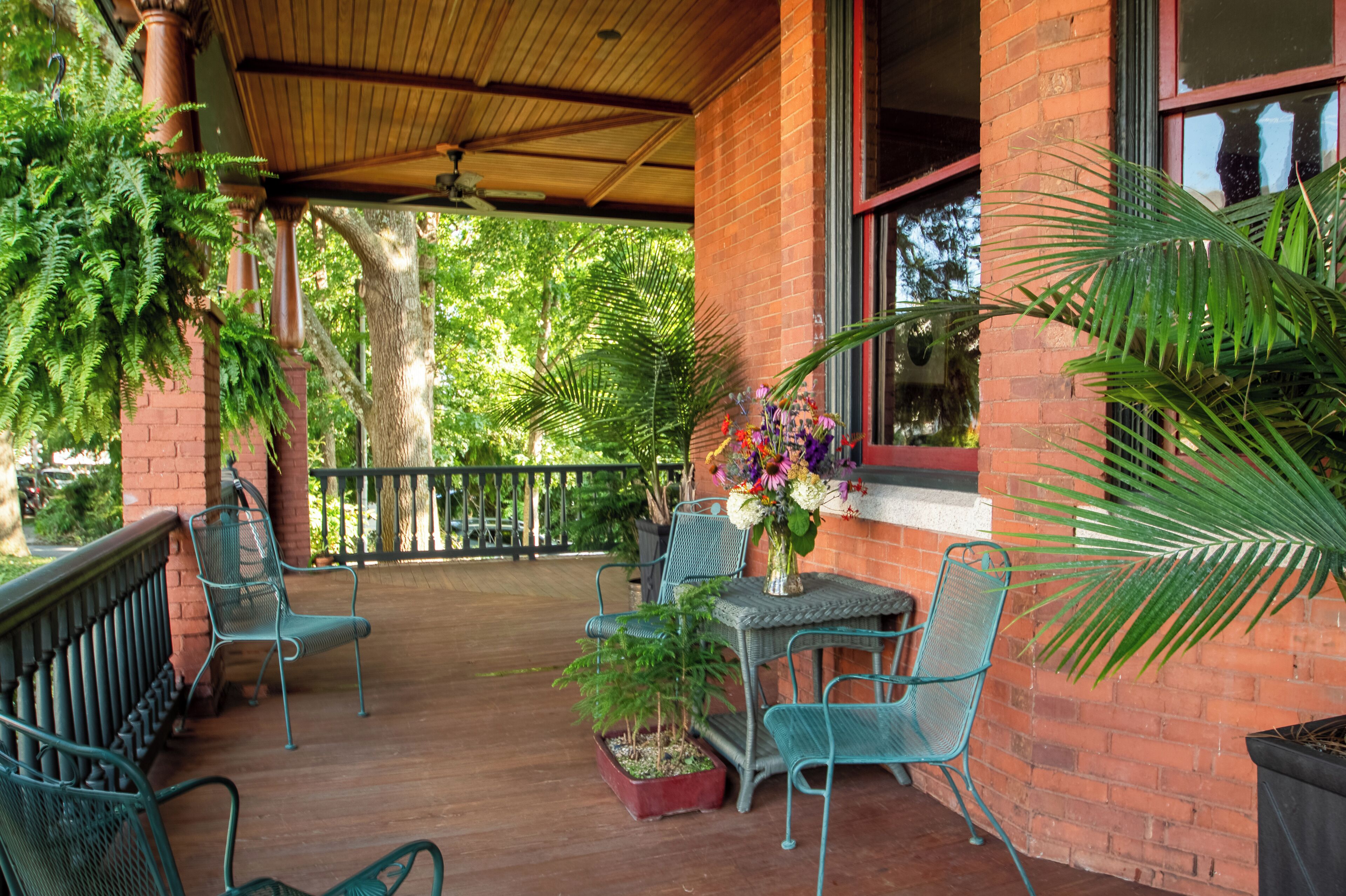 A covered patio area with brick walls, metal chairs, a table with a vase of flowers, and potted plants.