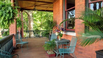 A covered patio area with brick walls, metal chairs, a table with a vase of flowers, and potted plants.