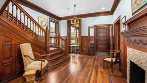 A spacious foyer with a wooden staircase, a fireplace, and a large window. - Summit Street Inns (Winston-Salem)